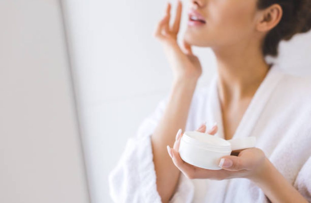 cropped shot of beautiful woman in bathrobe applying face cream